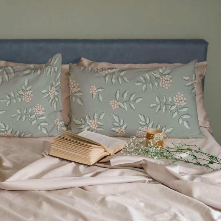 Soft sage pillowcases with pink rowan berry pattern on a cozy bed with open book and mug