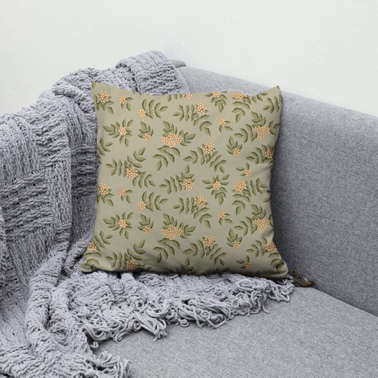 Square cushion with golden rowan berry pattern on green background, styled on a gray sofa with knit throw